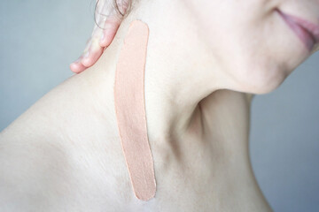 Naklejka premium Close-up of elastic beige kinesiology tape on female caucasian shoulder for muscle support and pain relief.