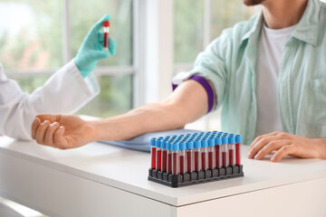 Test tubes with blood on table against donor and doctor in clinic, closeup