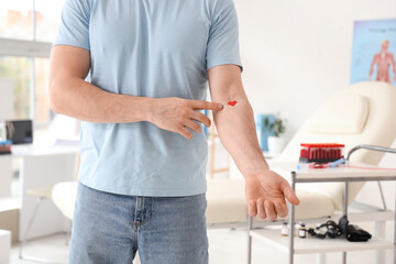 Young man pointing at applied patch after donating blood in clinic