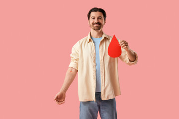 Male blood donor with medical patch and paper drop on pink background