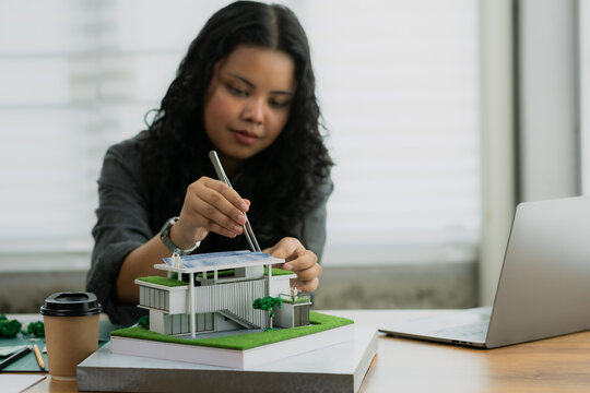 Using tweezers for precision, an architect adds miniature scale figures to the roof of a sustainable house model