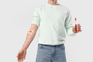 Male blood donor with medical patches and test tube on light background
