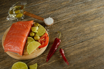 Meat red salmon fish, tomatoes, spices, lemon, green olives and olive oil on wooden kitchen table.