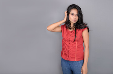 A confident young woman dressed casually in a red top and blue jeans, posing with jovial facial...