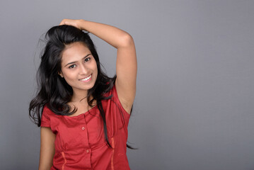 A confident young woman dressed casually in a red top and blue jeans, posing with jovial facial...