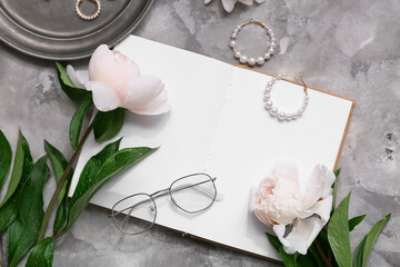 Composition with blank book, jewelry and peony flowers on grey grunge background, closeup