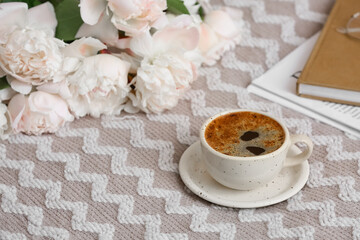 Cup of coffee with peony flowers on bed, closeup