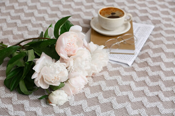 Cup of coffee with book, eyeglasses and peony flowers on bed, closeup