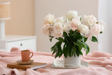 Tray with cup of coffee, peony flowers and books on bed