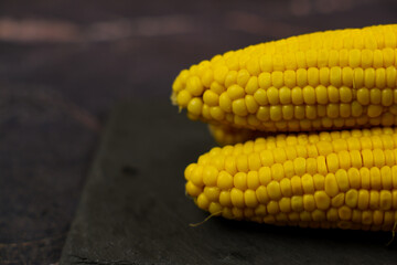 Close-up of yellow ripe peeled ears of corn with large grains lying on the side on a dark background with space for text. The concept of healthy nutrition, natural iron, corn cultivation. High quality
