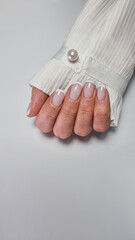 A close-up of a hand with a neat red French manicure on nails, set against a white background. The hand is partially covered by the sleeve of a white shirt, creating a clean and elegant look.