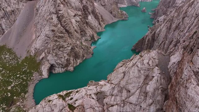 An aerial view captures the intense turquoise color of Kel Suu Lake, deeply embedded within a rugged gorge of towering rock cliffs