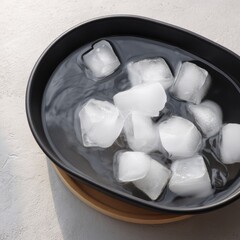 Black bowl with water and melting ice cubes on a light surface, illustrating cold temperature and refreshment concept.