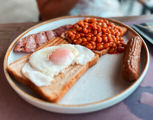 Modern british breakfast with eggs on a toast, beans, sausage and bacon
