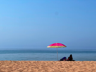 Single red umbrella on golden sandy beach with sea and bright sky in the background