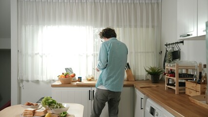 Happy father move to music while cooking food and prepare lunch at modern kitchen. Active dad dancing to song while making healthy food or salad surrounded with vegetable and kitchenware. Pedagogy.