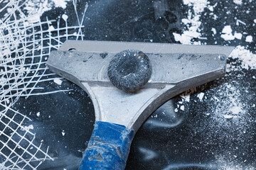 Close-up of a metal scraper lying on a dark surface surrounded by plaster debris and torn mesh, symbolizing plaster removal, surface preparation, and manual renovation work.