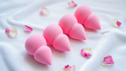 Obraz premium Pink beauty sponges and delicate rose petals on a soft white background for cosmetics.