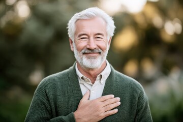 Elderly man with hand on chest smiling warmly in autumn park
