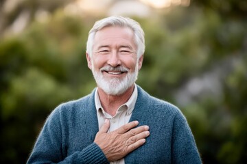 Smiling elderly man with hand on chest in golden hour park