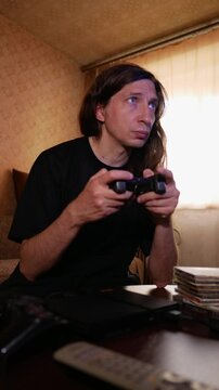 An intense and concentrated mood is captured as a man with long hair plays a video game using a controller, his profile sharply focused on the screen, reflecting deep immersion in the game
