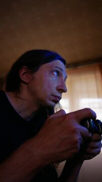 An intense and reactive mood is captured as a man with long hair, illuminated by the screen's glow, plays a video game
