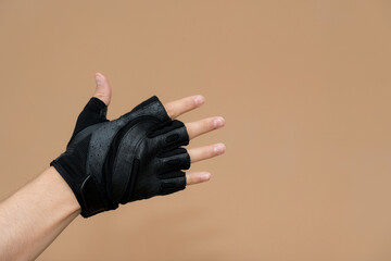 A hand wearing a black fingerless workout glove, extending outward against a solid gold/beige background