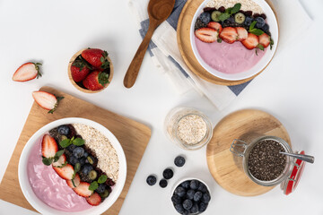 Presented by fruits putting yogurt toppings with strawberry, berry, oats, raisins and chia seed decorated by peppermint in white blow. Pink background. Set of healthy dairy product choice. Pecuniary.