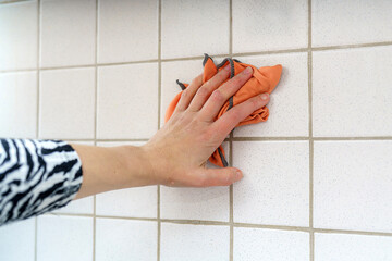 Hand cleaning tile wall with orange cloth in kitchen during daytime activity for improved...