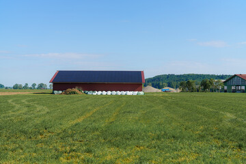Sunny day on a rural farm with a red barn and hay bales in the field