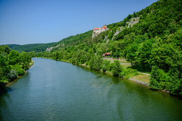 Scenic river surrounded by lush greenery and hills on a sunny day near a historical site