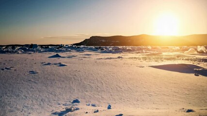 Shards of translucent ice scattered on a frozen landscape against the rising sun on a winter morning near a dark hill - Powered by Adobe