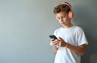 Fototapeta premium Teen boy wearing headphones using smartphone. Young man listens music app. Teenager with mobile phone, modern tech device. Student listening audiobook, podcast against wall. Teenager, music lover,