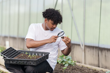 teenage multiracial male student of African descent holding magnifying glass closely inspecting...
