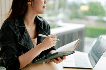 Obraz premium Beautiful Asian woman sitting working on laptop in coffee shop. Freelance translator. Young woman studying online.