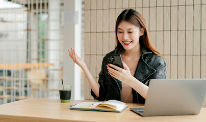 Beautiful Asian woman holding smartphone, typing text, chatting with friends, video calling on...