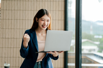 Cheerful Asian businesswoman stands holding laptop at office, financial report analysis, investment...