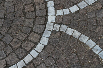 Contrast of grey and white cobblestones on textured pavement surface.
