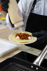 chef elaborando un burrito de tiras de carne salsa y mayonesa y sus manos con guantes para manipular la comida
