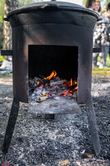 Fire Burns Brightly in a Rustic Metal Stove While Wood is Added for Cooking Outdoors in a Natural...