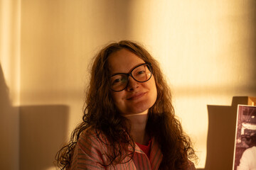 Portrait of a young woman with curly hair and eyeglasses, smiling brightly while basking in the...