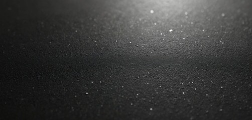 Dark rough surface with grainy texture. Black background features tiny shining particles. Abstract grunge design for backgrounds, patterns, templates. Rough, rugged, uneven surface.