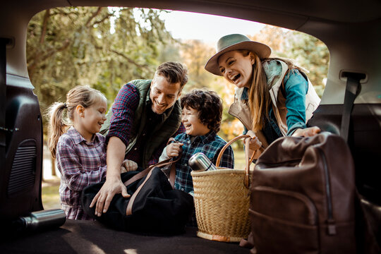 Happy family packing car trunk for weekend road trip with kids