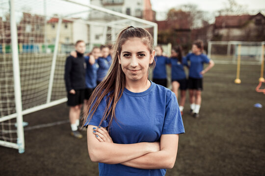 Confident girl soccer player posing in front of team on field