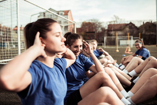 Teenage female soccer team performing sit ups during training on football field - Powered by Adobe