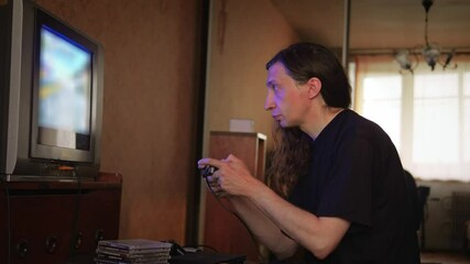 An intensely concentrated and nostalgic mood is captured as a man with long hair plays a video game on an older television set, his profile sharply focused on the screen