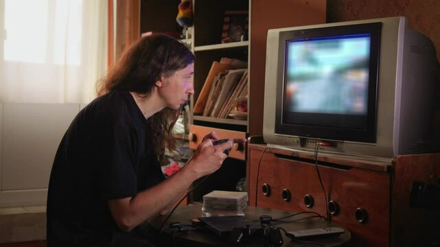 An intensely concentrated and nostalgic mood is captured as a man with long hair plays a video game on an older television set, his profile sharply focused on the screen