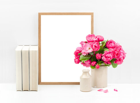 feminine mockup with wooden picture / photo frame, cream colored books and a bunch of roses in a vase on a white shelf or desk against a bright wall, just insert your artwork, poster or photo, PNG 
