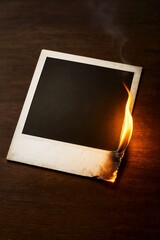 Burning instant polaroid photo frame on dark wood surface.  Old instant photo is burning with small flame. Blank instant photo frame burning for military secrecy concept.