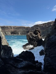 Dramatic Coastal Rocks Framing Turquoise Ocean Waves and White Foam Under Blue Sky, Hidden Seaside...